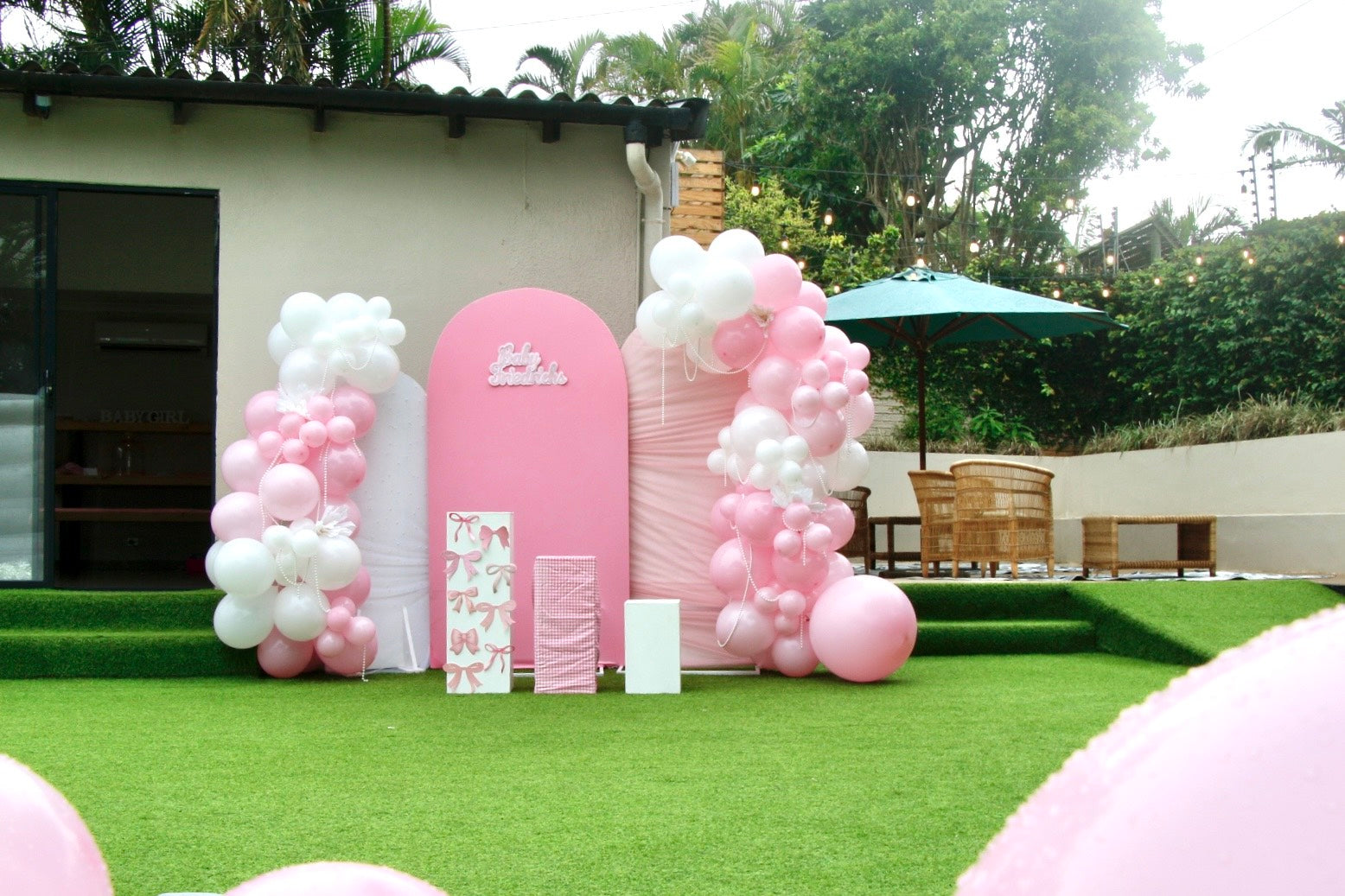 Pink archway with balloons and a sign in an outdoor setting